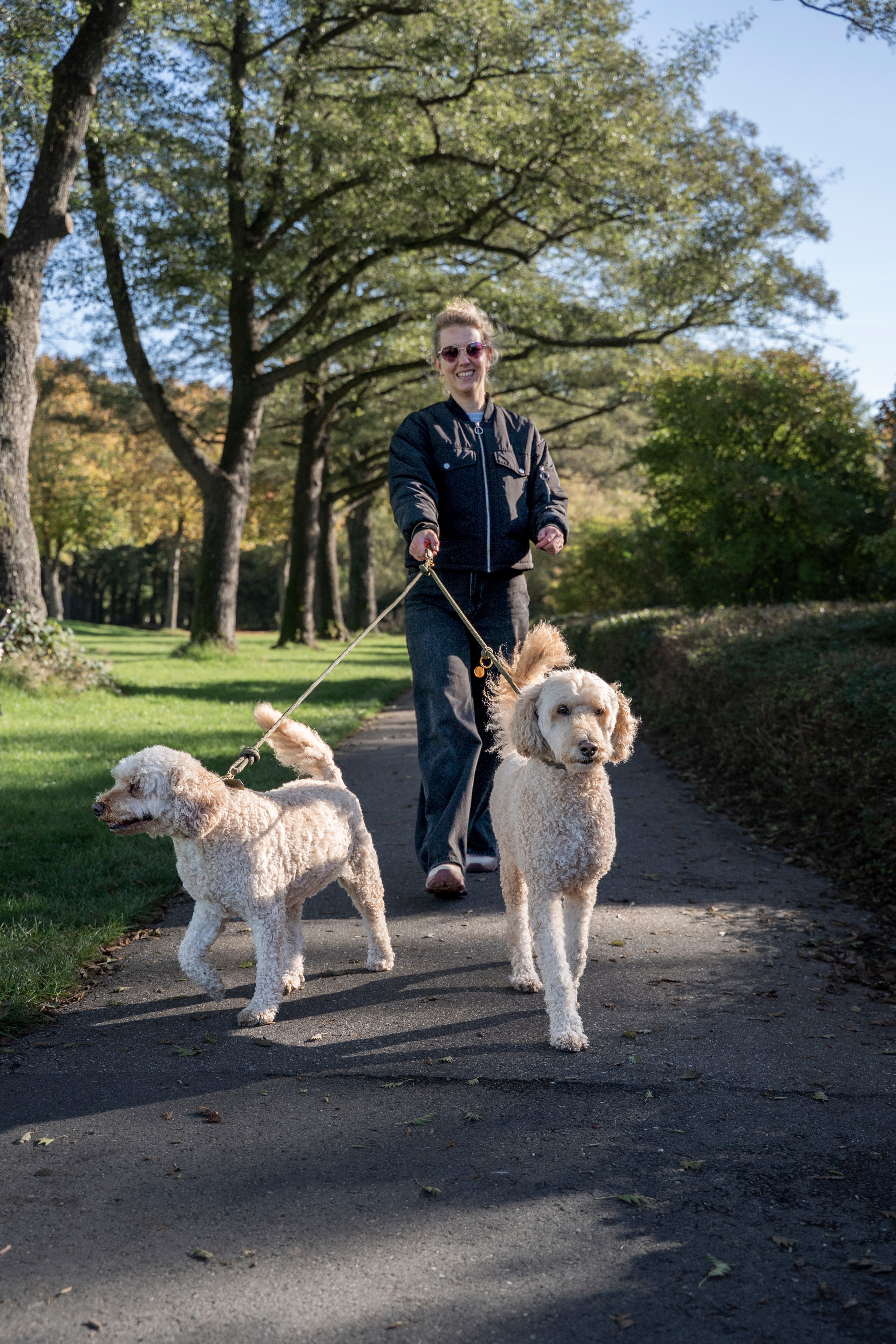 vrouw loopt met 2 labradoodles aan de multifunctionele paracord lijn van punq. ze gebruikt ook de losse handlus